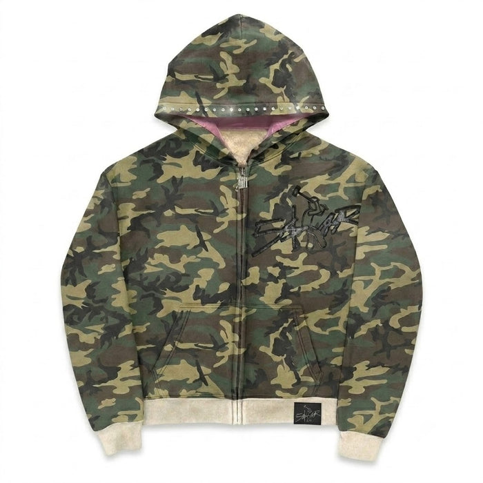 A Stussy camouflage zip-up hoodie with a green, brown, and tan camo pattern, featuring a black Stussy logo on the chest, a pink inner hood lining, and beige ribbed cuffs and hem.