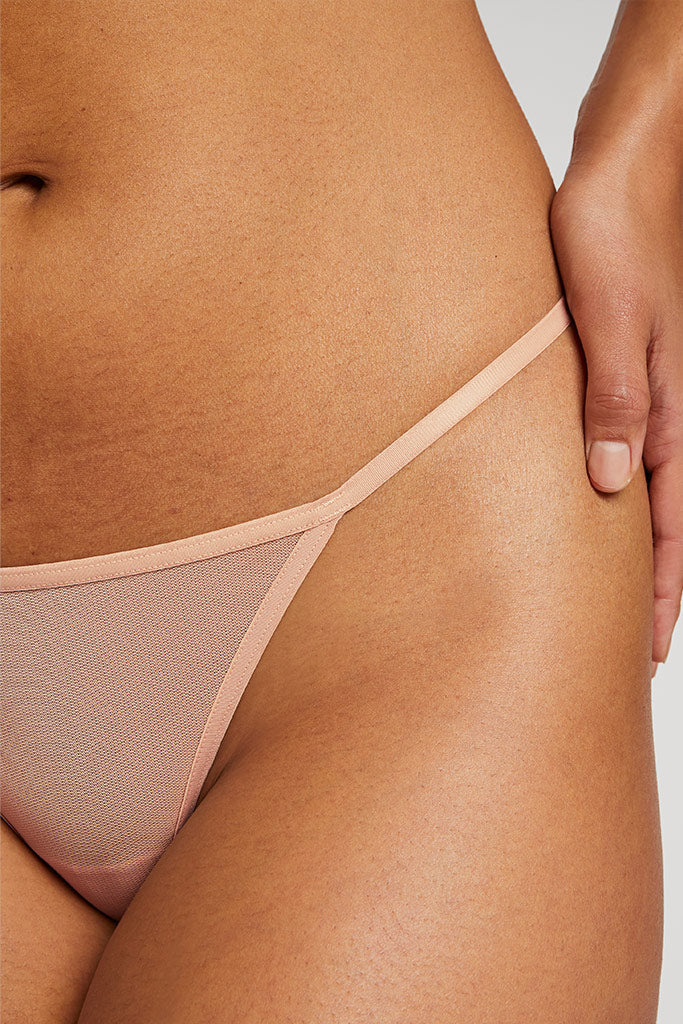 Close-up of a person wearing a beige thong against a neutral background
